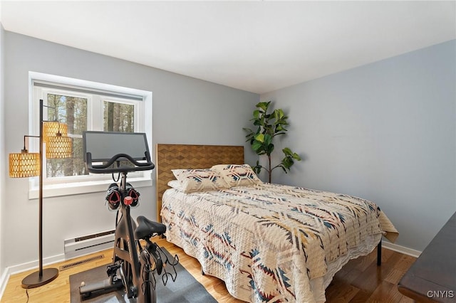 bedroom featuring baseboard heating, wood finished floors, visible vents, and baseboards