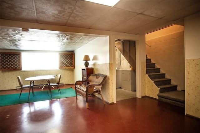 living area with stairs, concrete block wall, baseboard heating, concrete flooring, and wallpapered walls