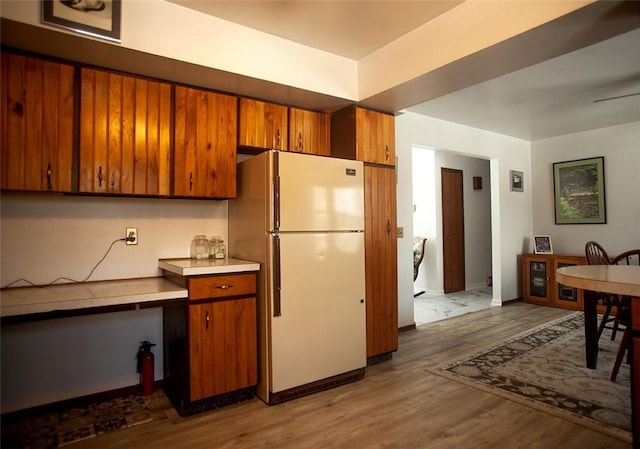 kitchen with light countertops, wood finished floors, freestanding refrigerator, and brown cabinets