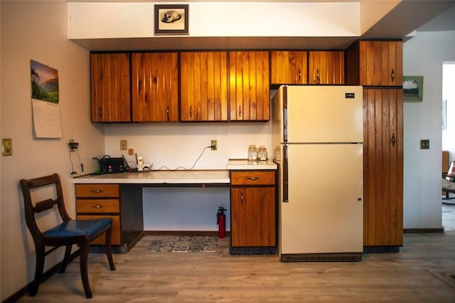 kitchen with brown cabinetry, freestanding refrigerator, light countertops, and wood finished floors