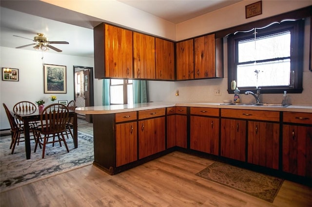 kitchen with a peninsula, light wood-type flooring, light countertops, and a sink