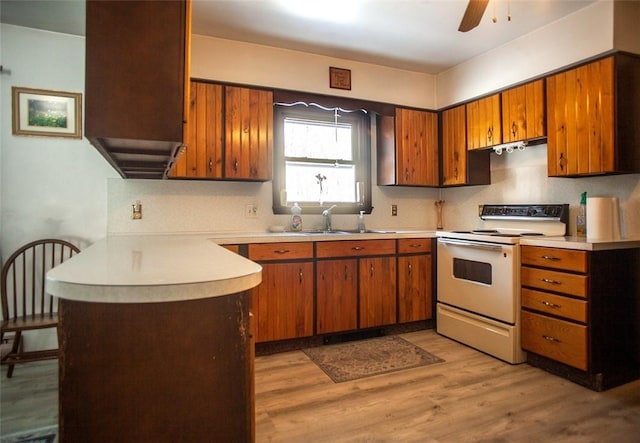 kitchen featuring white electric stove, a sink, light countertops, light wood-type flooring, and brown cabinetry