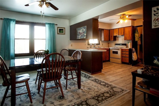 kitchen featuring white range with electric stovetop, brown cabinets, light countertops, light wood-style flooring, and a peninsula