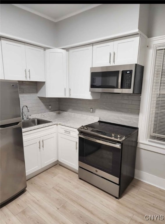 kitchen with white cabinets, crown molding, stainless steel appliances, and a sink