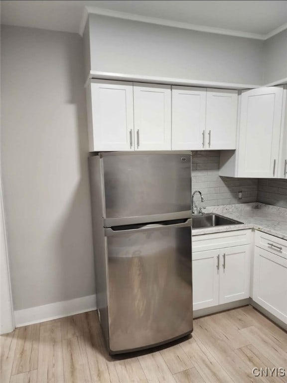 kitchen featuring light wood finished floors, backsplash, freestanding refrigerator, white cabinets, and a sink