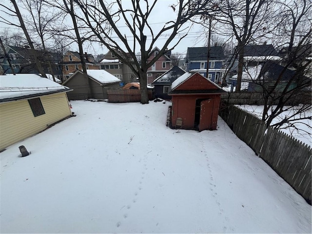 yard covered in snow with a storage shed, a residential view, fence, and an outdoor structure