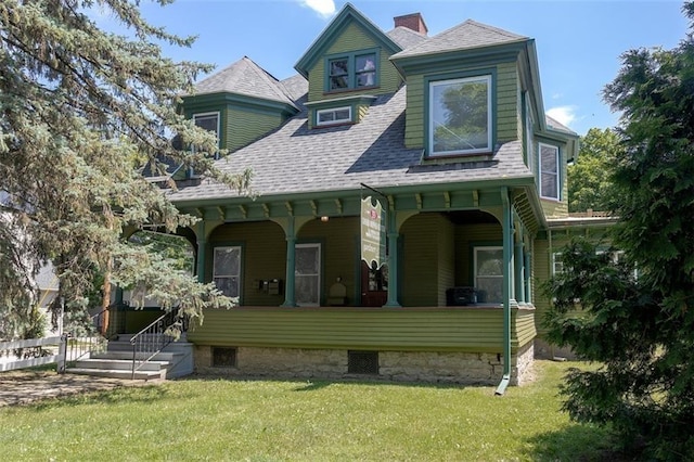 view of front facade with covered porch, a shingled roof, and a front yard