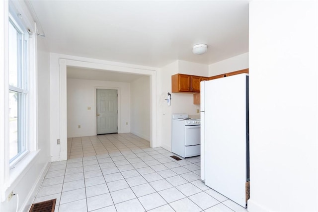 kitchen with brown cabinets, visible vents, light tile patterned flooring, white appliances, and baseboards