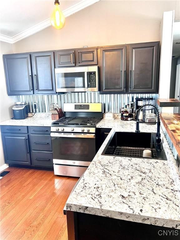 kitchen with stainless steel appliances, light countertops, ornamental molding, vaulted ceiling, and a sink