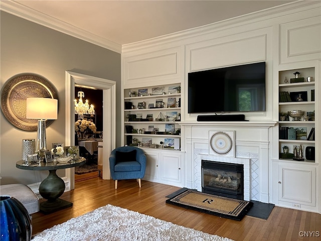 living room with ornamental molding, a tile fireplace, wood finished floors, and built in shelves