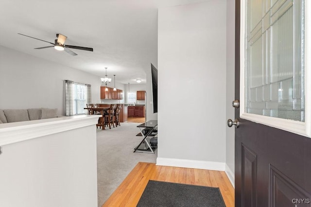 entryway with ceiling fan with notable chandelier, light wood finished floors, light carpet, and baseboards