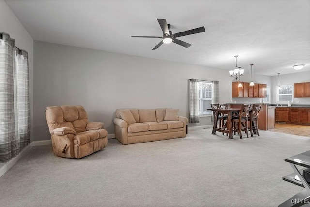 living area featuring ceiling fan with notable chandelier, baseboards, and light colored carpet