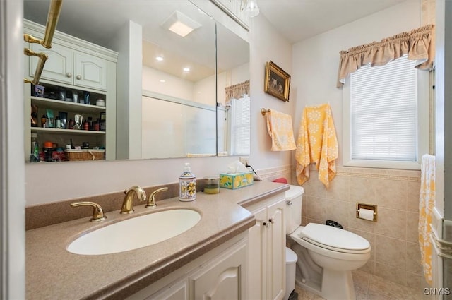 bathroom featuring a shower with shower door, toilet, a wainscoted wall, vanity, and tile walls