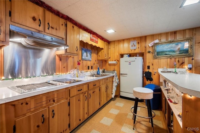 kitchen featuring light floors, freestanding refrigerator, light countertops, under cabinet range hood, and a sink