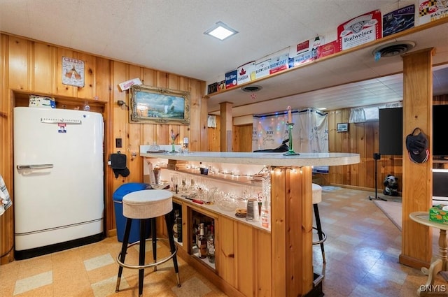 bar featuring a dry bar, visible vents, freestanding refrigerator, wood walls, and tile patterned floors