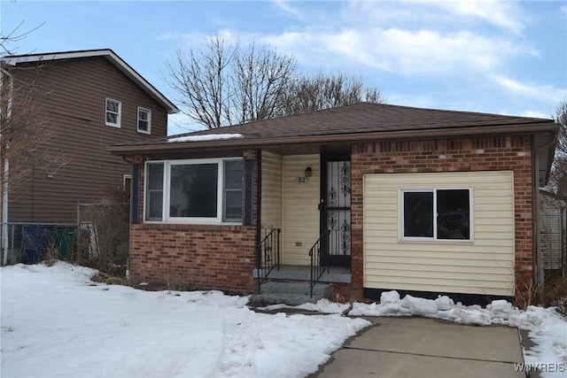 view of front of house featuring a shingled roof, brick siding, and fence