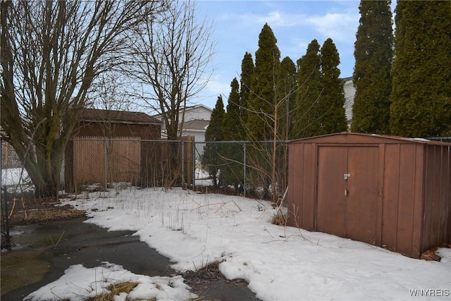 yard covered in snow with a storage shed, fence, and an outbuilding