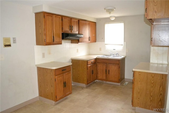 kitchen featuring a sink, tasteful backsplash, brown cabinets, and under cabinet range hood