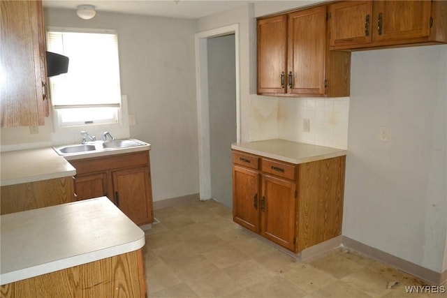 kitchen featuring decorative backsplash, brown cabinets, light countertops, light floors, and a sink