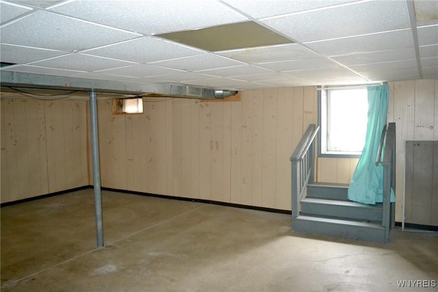 below grade area with stairway, a drop ceiling, and wooden walls