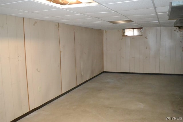 finished basement featuring a drop ceiling and wooden walls