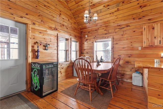 dining room featuring light wood finished floors, vaulted ceiling, and wood walls