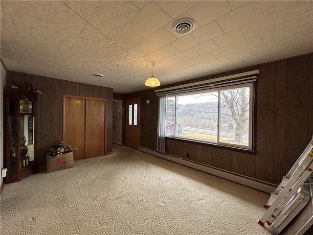 interior space with visible vents, carpet flooring, wooden walls, and a baseboard radiator