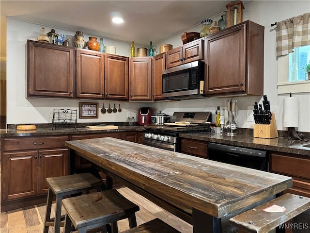 kitchen featuring appliances with stainless steel finishes, dark stone counters, and light wood-style floors