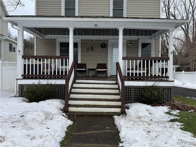 snow covered property entrance with covered porch and fence