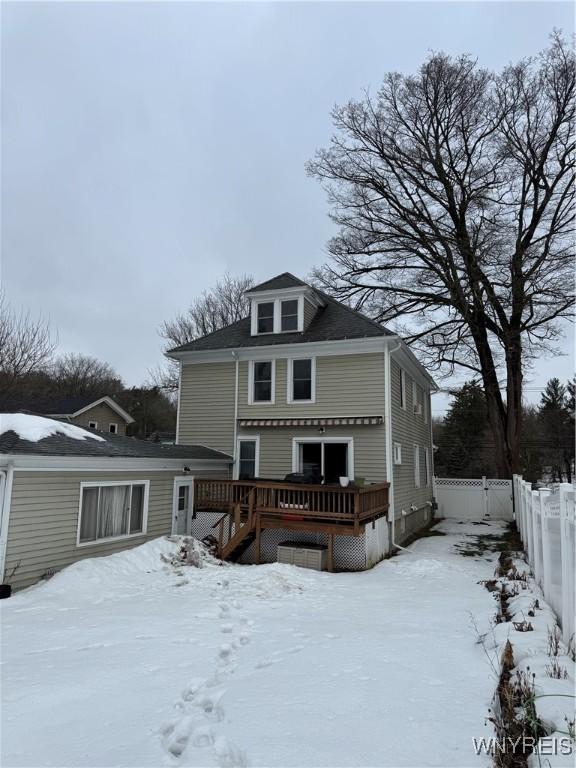 snow covered back of property featuring fence and a wooden deck