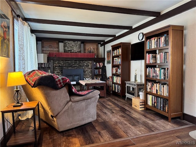 sitting room with beam ceiling, baseboards, wood finished floors, and a stone fireplace