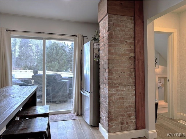 unfurnished dining area featuring light wood-type flooring, brick wall, and baseboards