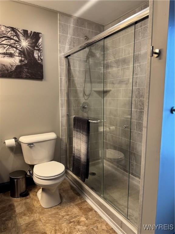 bathroom featuring toilet, a stall shower, and baseboards