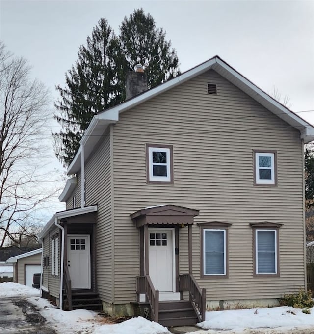 view of front of property with entry steps, a chimney, a detached garage, and an outbuilding