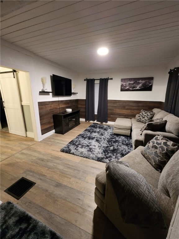 living room with a barn door, a wainscoted wall, wood walls, wood finished floors, and visible vents