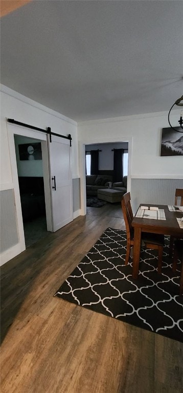 dining space with ornamental molding, wood finished floors, a wainscoted wall, and a barn door