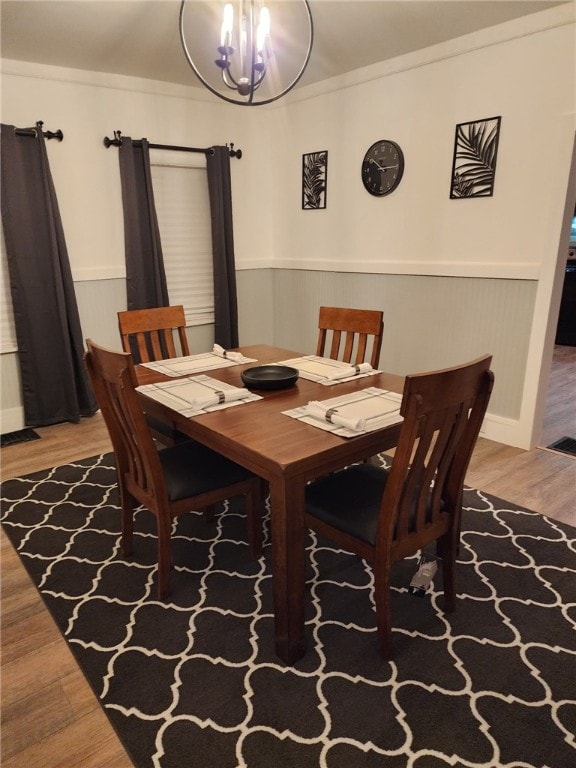 dining room with a wainscoted wall, a chandelier, crown molding, and wood finished floors