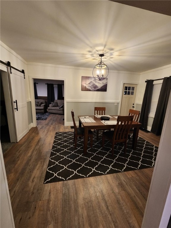 dining room featuring ornamental molding, a barn door, dark wood-style flooring, and a chandelier