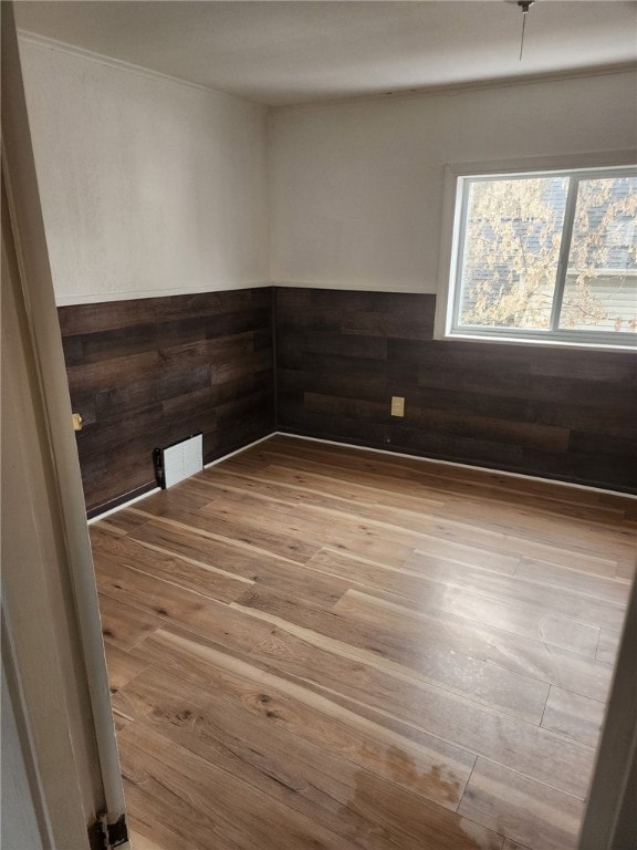 empty room featuring wood walls, wainscoting, and wood finished floors