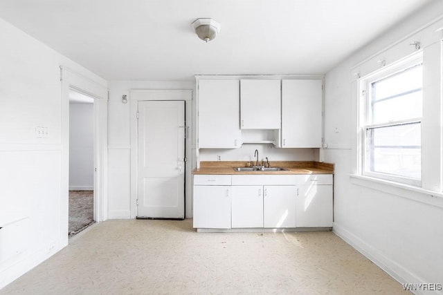 kitchen featuring baseboards, light countertops, a sink, and white cabinets