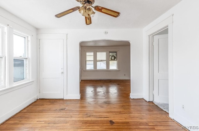 unfurnished room with baseboards, light wood-style floors, a ceiling fan, and a healthy amount of sunlight