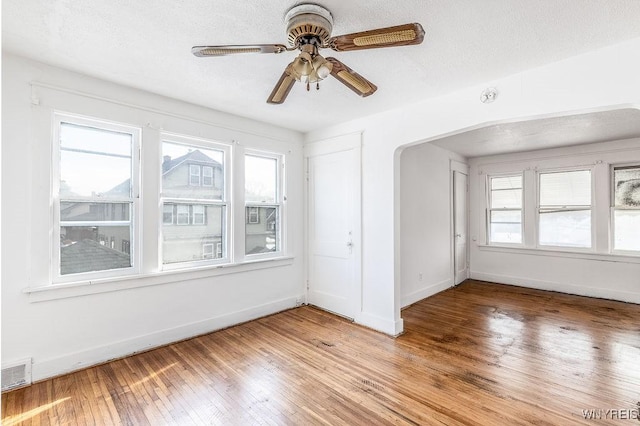 unfurnished room featuring light wood-style flooring, visible vents, arched walkways, and baseboards