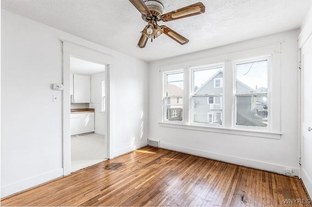 spare room featuring visible vents, light wood-style flooring, a ceiling fan, a textured ceiling, and baseboards