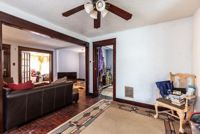 living area featuring baseboards, visible vents, ceiling fan, wood finished floors, and a textured ceiling