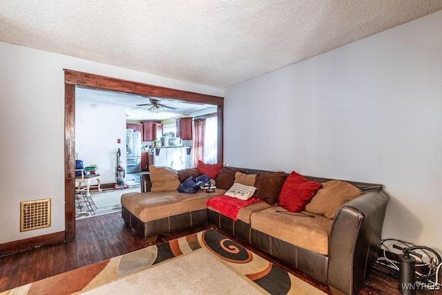 living area with a textured ceiling, wood finished floors, visible vents, and baseboards