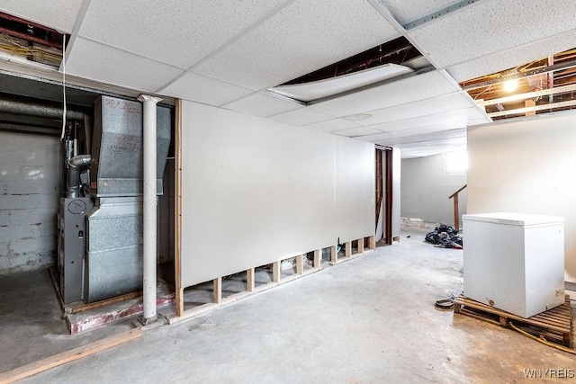 below grade area with a paneled ceiling, concrete block wall, and fridge