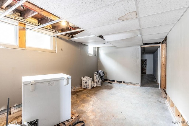 basement with a drop ceiling and fridge