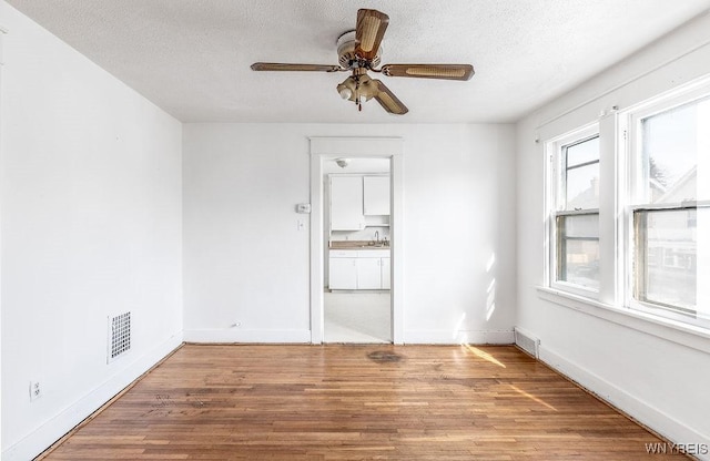 unfurnished room with a textured ceiling, wood finished floors, visible vents, and baseboards