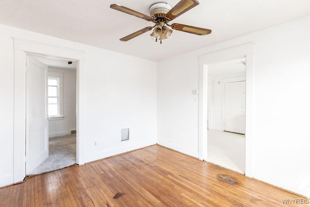 empty room featuring ceiling fan, light wood-style flooring, visible vents, and baseboards