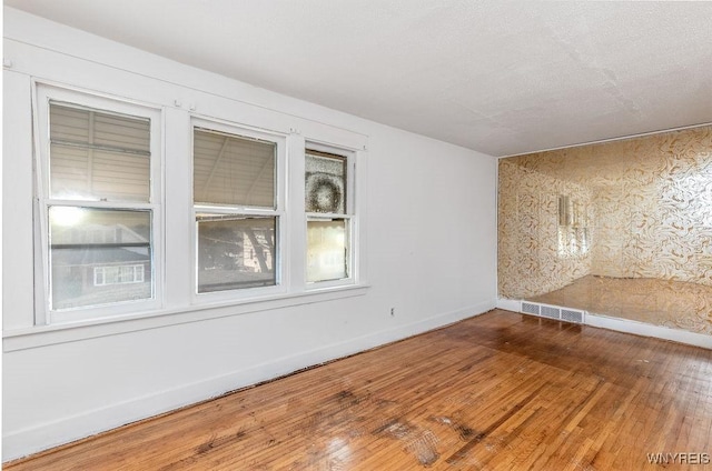 unfurnished room featuring wood-type flooring, visible vents, and baseboards